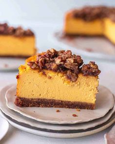 a slice of pumpkin cheesecake with pecans on top and two plates in the background