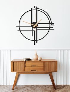 a modern clock on the wall above a table with a vase and book in front of it