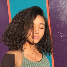 a woman with curly hair standing in front of a purple and blue wall