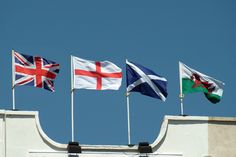 four flags flying in the wind on top of a building