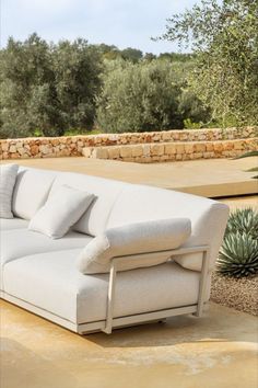 a white couch sitting on top of a cement floor next to an olive tree and stone wall