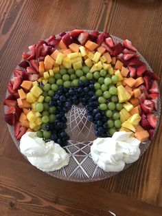 a rainbow shaped fruit platter with whipped cream and berries on the side, sitting on a wooden table