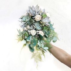 a bouquet of succulents and roses is being held by someone's hand