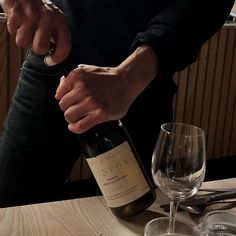 a person pouring wine into a glass on top of a wooden table with silverware and utensils