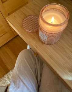 a candle sitting on top of a wooden table next to a person's legs