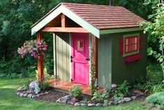 a small garden shed in the middle of some grass and trees with flowers around it