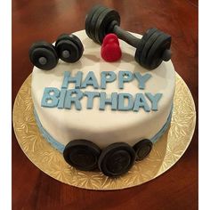 a birthday cake with dumbbells and the words happy birthday written on it is sitting on a table