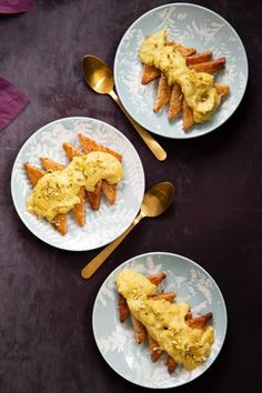 two white plates topped with food on top of a black table next to gold spoons