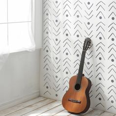 an acoustic guitar leaning against a wall in front of a patterned wallpapered background