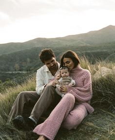 a man and woman are sitting in the grass with a baby