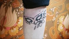 a black and white tattoo on the leg of a person wearing a butterfly mask with flowers around it