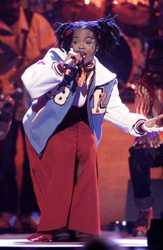 a woman in red pants and white jacket on stage with her hands out to the side