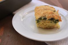 a piece of food on a plate next to a casserole dish with cheese and spinach