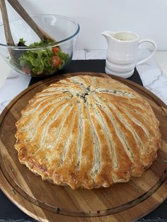 a pie sitting on top of a wooden platter next to a bowl of salad