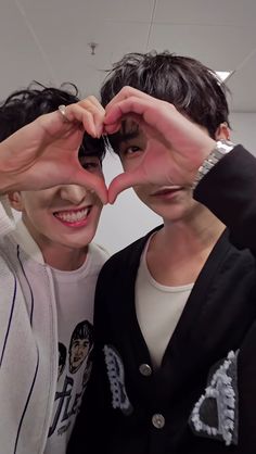 two people making a heart shape with their hands in front of the camera while standing next to each other