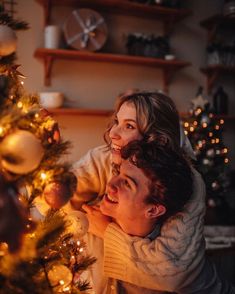 a man and woman are sitting in front of a christmas tree with lights on it