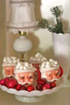 three santa clause heads sitting on top of a white bowl filled with balls and candy