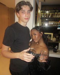 a man and woman standing next to each other in front of a counter with wine glasses