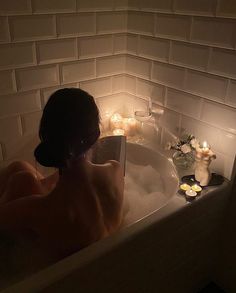 a woman sitting in a bathtub with candles on the side and flowers around her