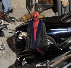 a man in a red and black suit standing next to cars