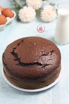 a chocolate cake sitting on top of a white plate next to some eggs and milk