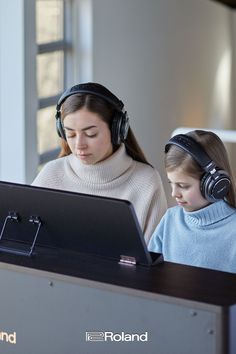 two girls wearing headphones are looking at a laptop