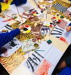 children are painting with animal prints on paper and watercolors at a table that is set up for an art class