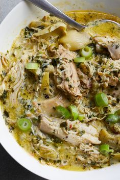 a white bowl filled with meat and vegetables next to a spoon on top of a table