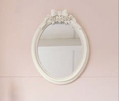 a white oval mirror hanging on the wall above a sink in a room with pink walls