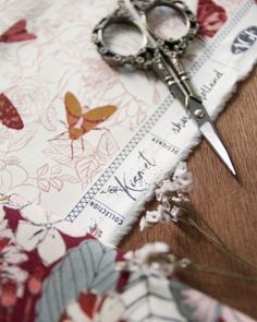 a pair of scissors sitting on top of a piece of fabric next to some flowers