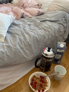 a bowl of granola next to a cup of coffee on the floor in front of a bed