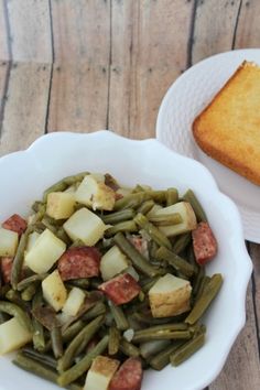 there is a bowl of green beans and potatoes next to a slice of toasted bread