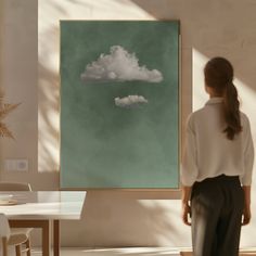 a woman standing in front of a painting on the wall with clouds floating above it