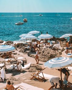 many people are on the beach with umbrellas and lounge chairs in front of the water