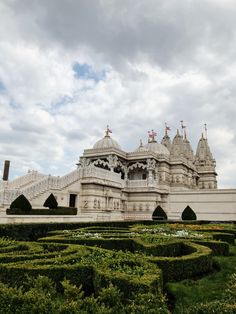 a large white building surrounded by hedges and bushes on a cloudy day with blue sky in the background