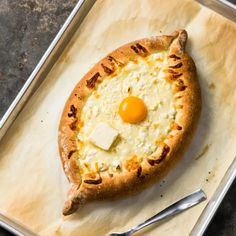 a pizza with an egg on it sitting on top of a pan next to a fork and knife