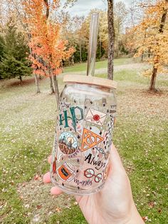 a hand holding up a glass with stickers on it and trees in the background