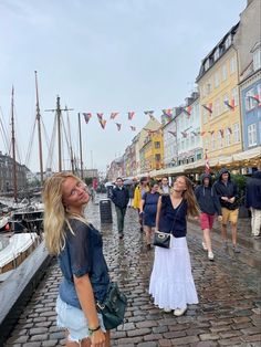 a group of people walking down a cobblestone road next to buildings and boats