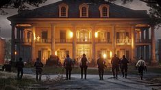 a group of people standing in front of a large house at night with the lights on