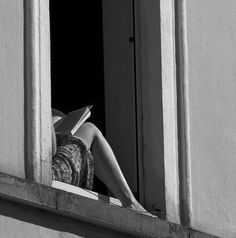 a woman reading a book while sitting in a window sill