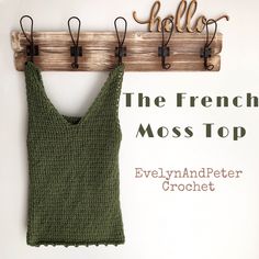 a knitted tank top hanging on a wooden coat rack with the words, the french moss top written in cursive font