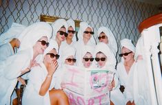 a group of women in white robes and sunglasses reading a newspaper