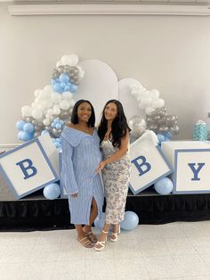 two women standing next to each other in front of a backdrop with balloons and letters