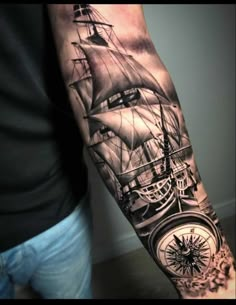 a man's arm with a ship, compass and clock tattoo on the sleeve