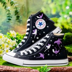 black and white high top converse sneakers with purple unicorns on them, surrounded by flowers