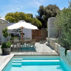 an outdoor swimming pool surrounded by wooden decking and patio furniture with umbrella over it