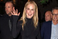 a woman in a black dress waves to the crowd