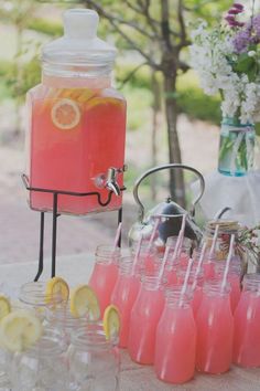 a table topped with lots of glasses filled with pink liquid and lemons next to a beverage dispenser