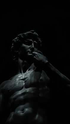 a statue is shown in the dark with no shirt on and his hands to his face