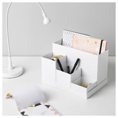 an office desk set with pen, paper and pencils in it next to a lamp